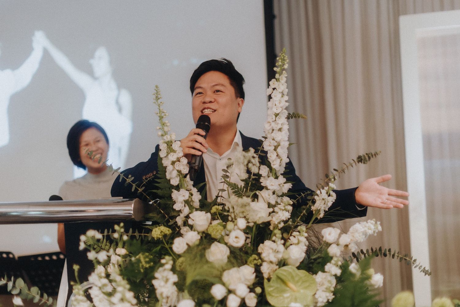 Wedding celebration scene with elegant white floral arrangements and decor in a light-filled venue.
