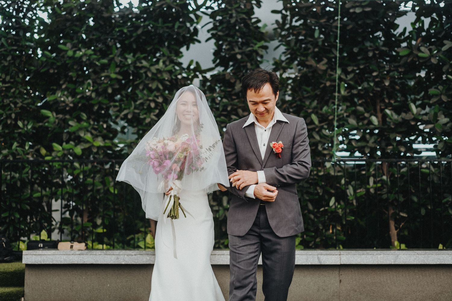 A wedding couple stands together outdoors with trees in the background during their ceremony.
