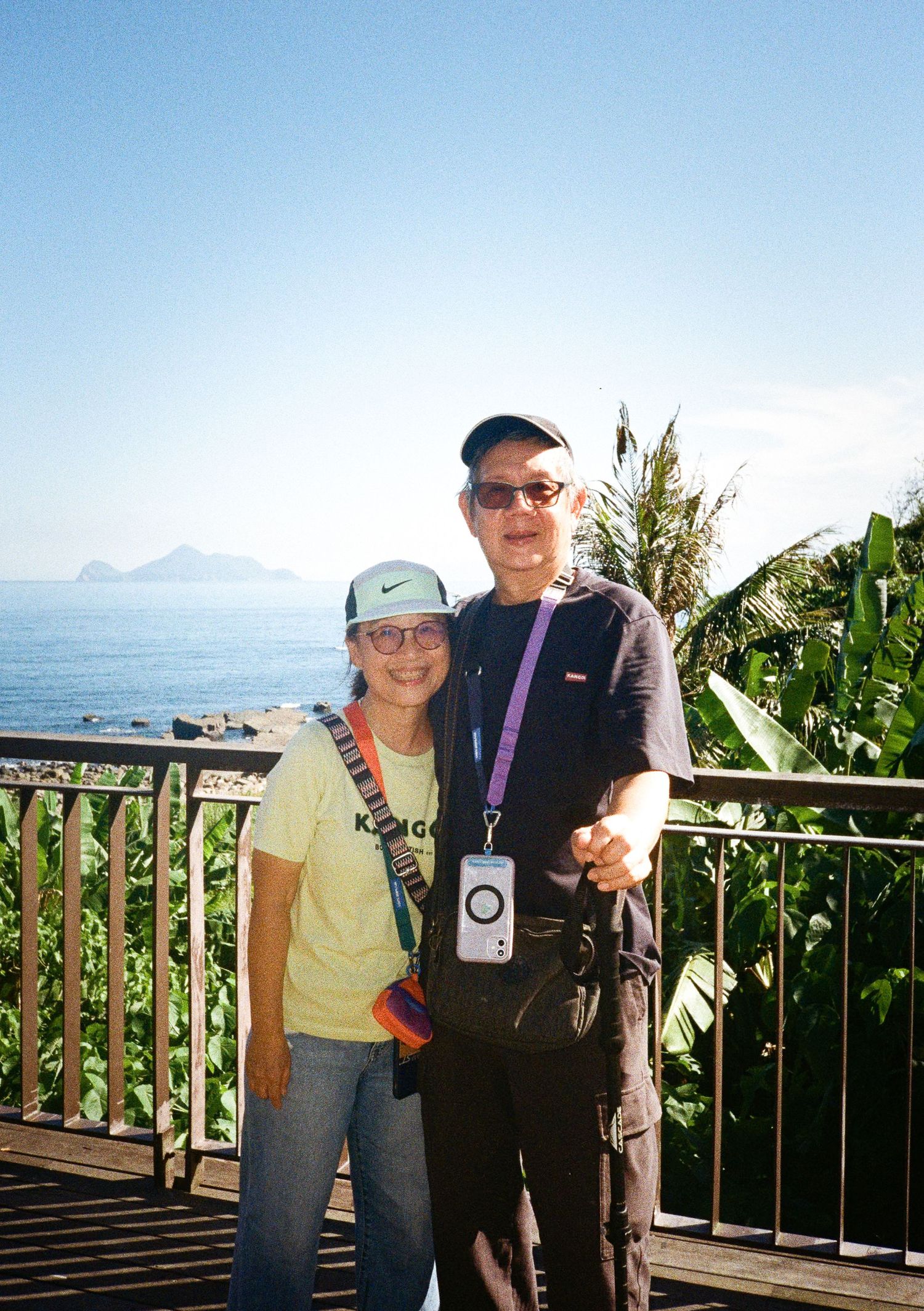 People posing together on an outdoor balcony or viewing area with mountains and ocean in the background.