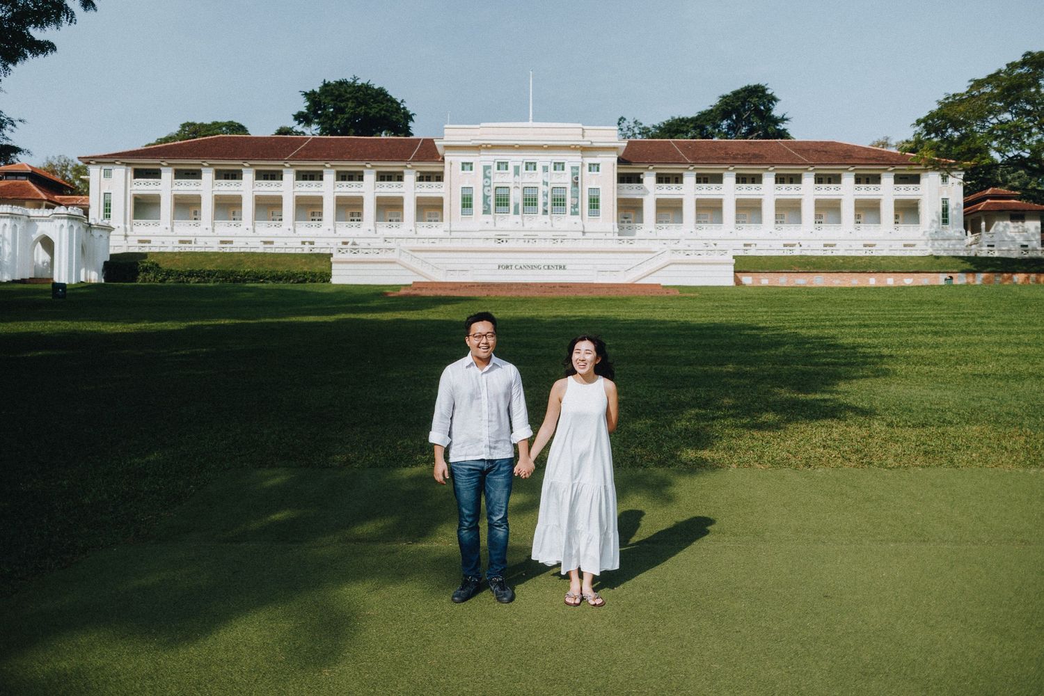 A couple walks across a manicured lawn with a white colonial building in the background.