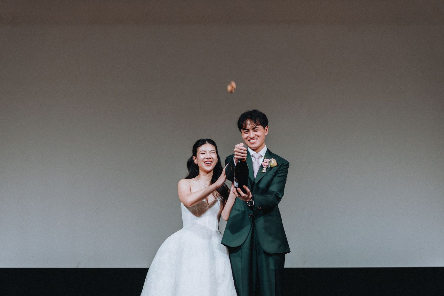 A smiling bride and groom pop a champagne bottle with sparks flying at their wedding celebration.