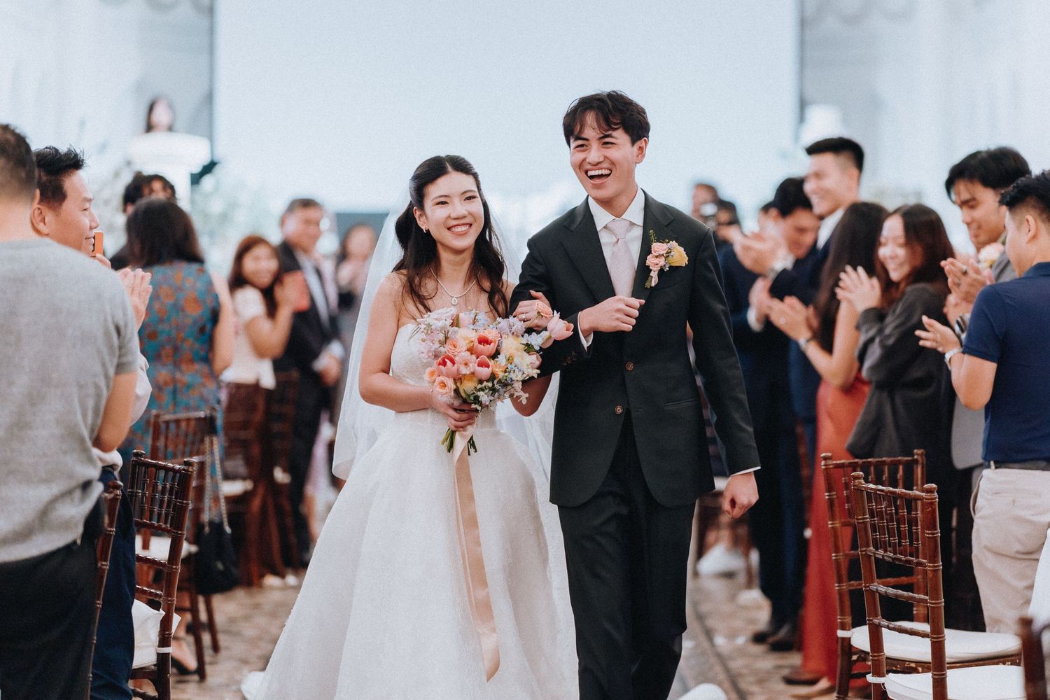 Happy newlywed Asian couple walking down the aisle after wedding ceremony.