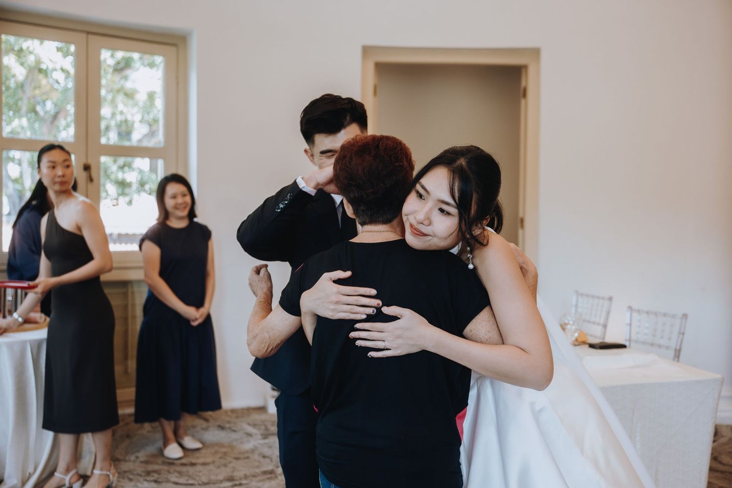 Bride and groom share warm embraces with wedding guests in bright elegant venue.