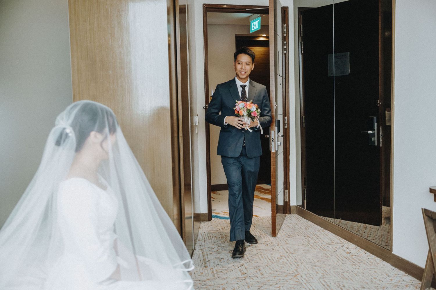 Groom in navy suit entering room with bouquet for bride's first look.