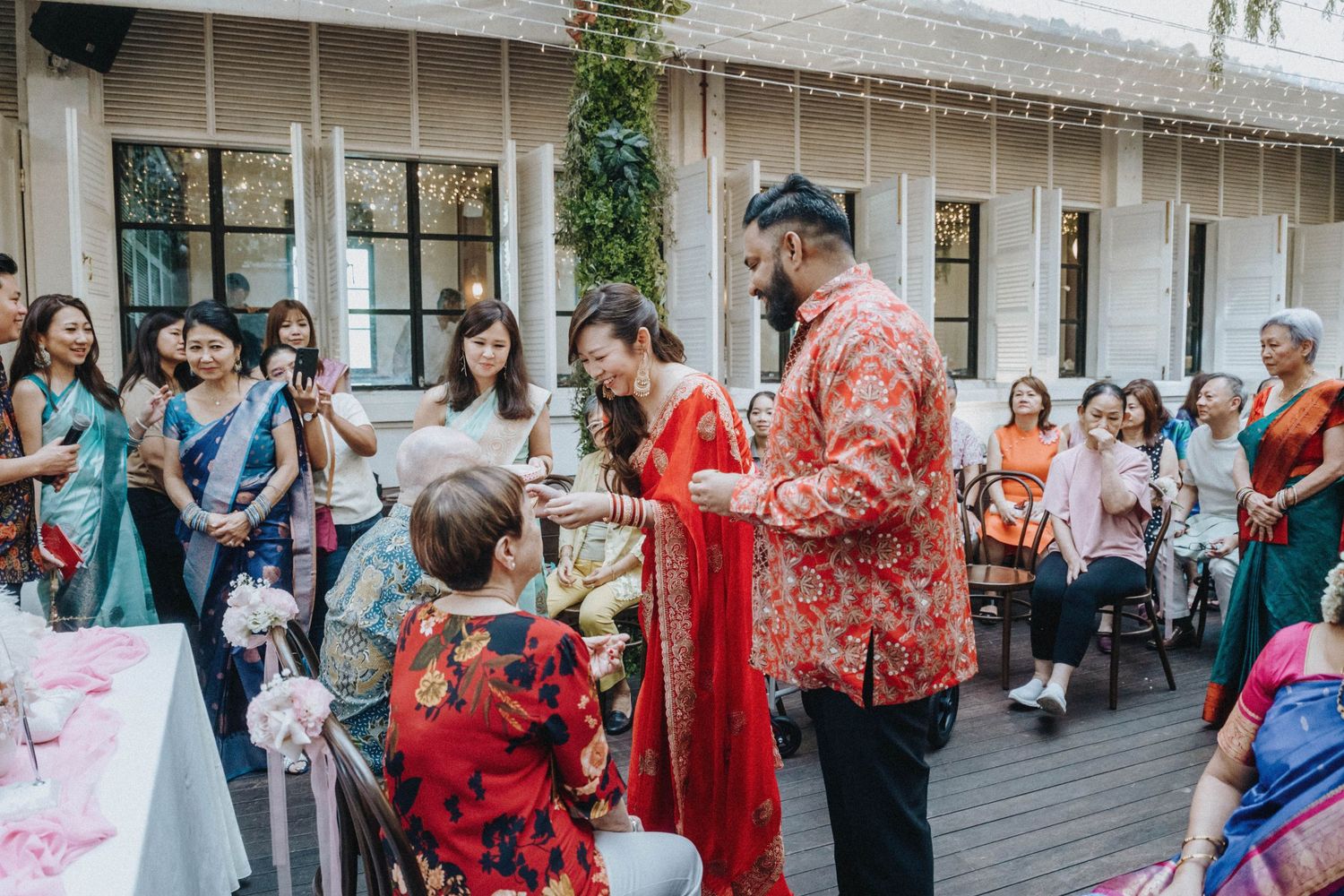 Guests in colorful traditional attire gather outdoors during a multicultural wedding ceremony celebration.