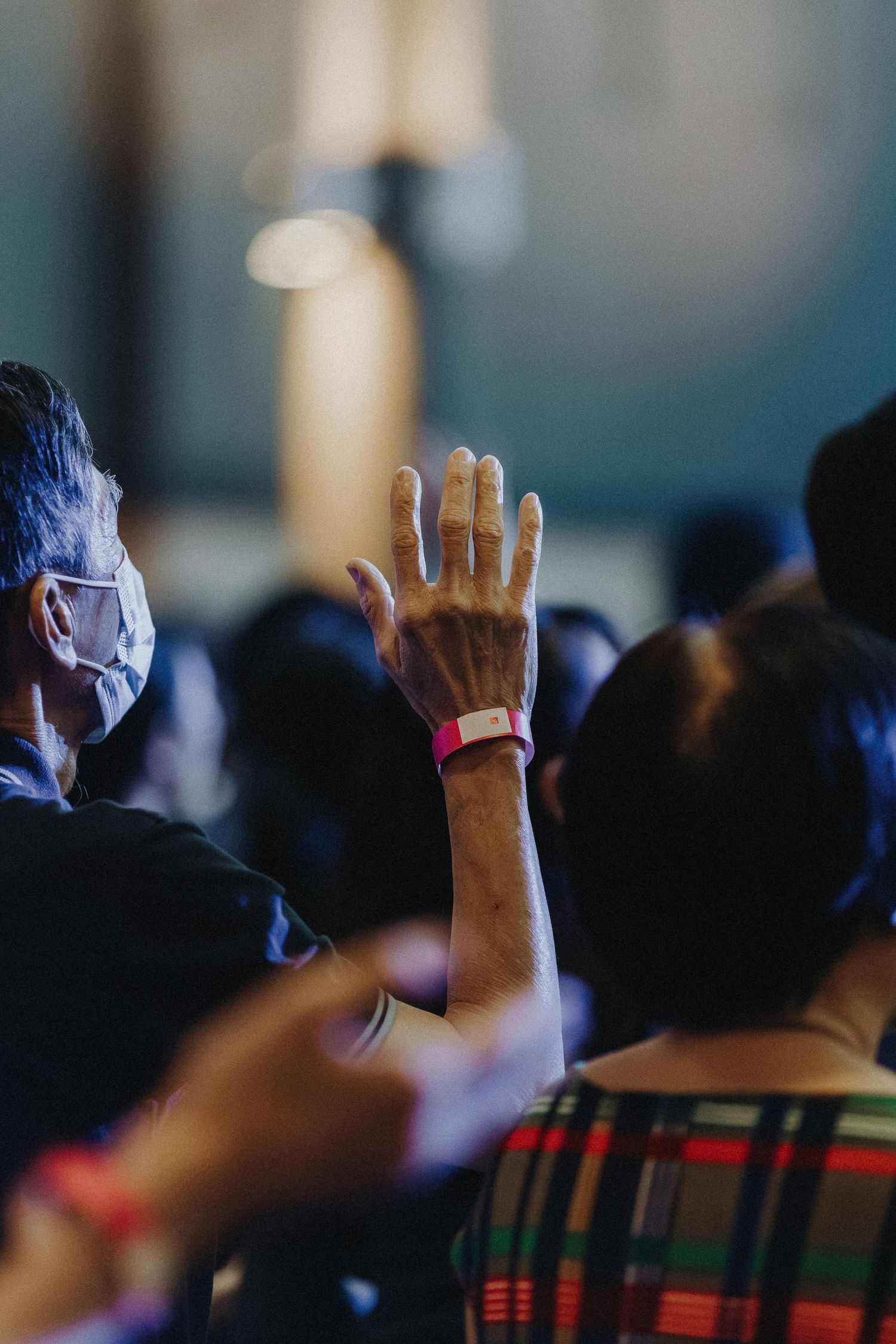 A raised hand with a wristband emerges from a crowd of concert attendees.