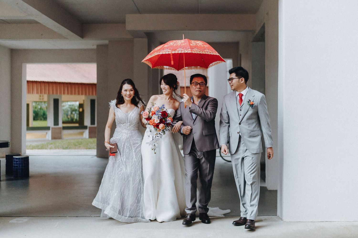 Wedding party walking together under a red umbrella in a covered walkway.