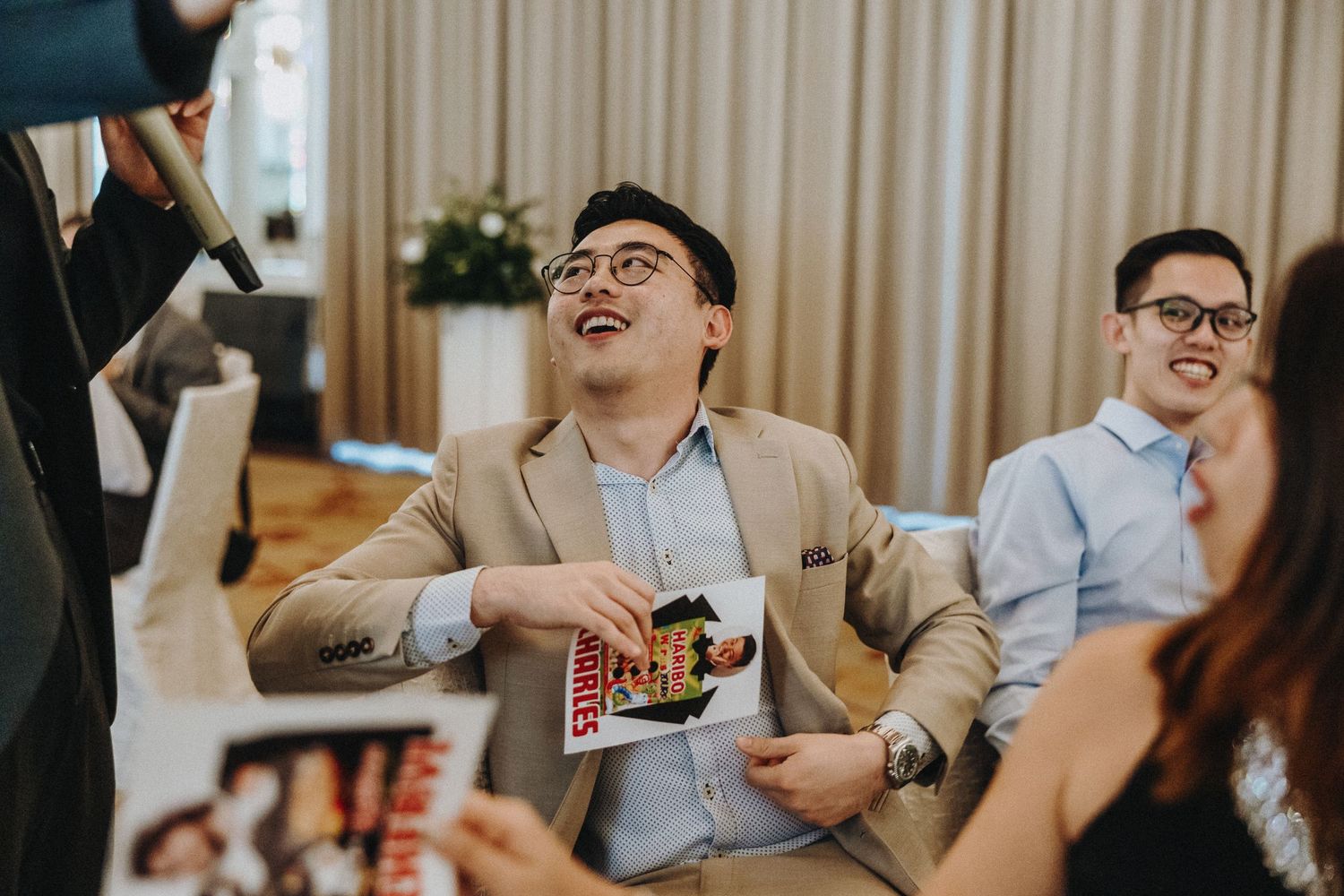 Wedding guests laughing and celebrating at reception while holding snacks and drinks.