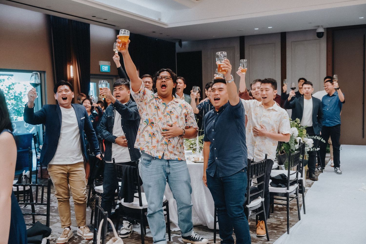 Wedding guests cheering and raising glasses during reception celebration indoors.