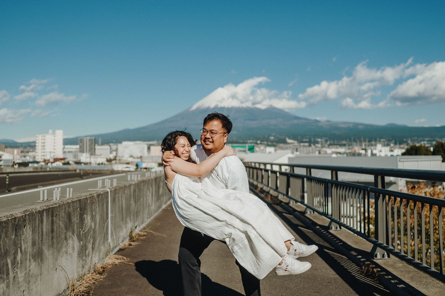 A joyful couple embraces on a rooftop with mountains and city buildings in the background.