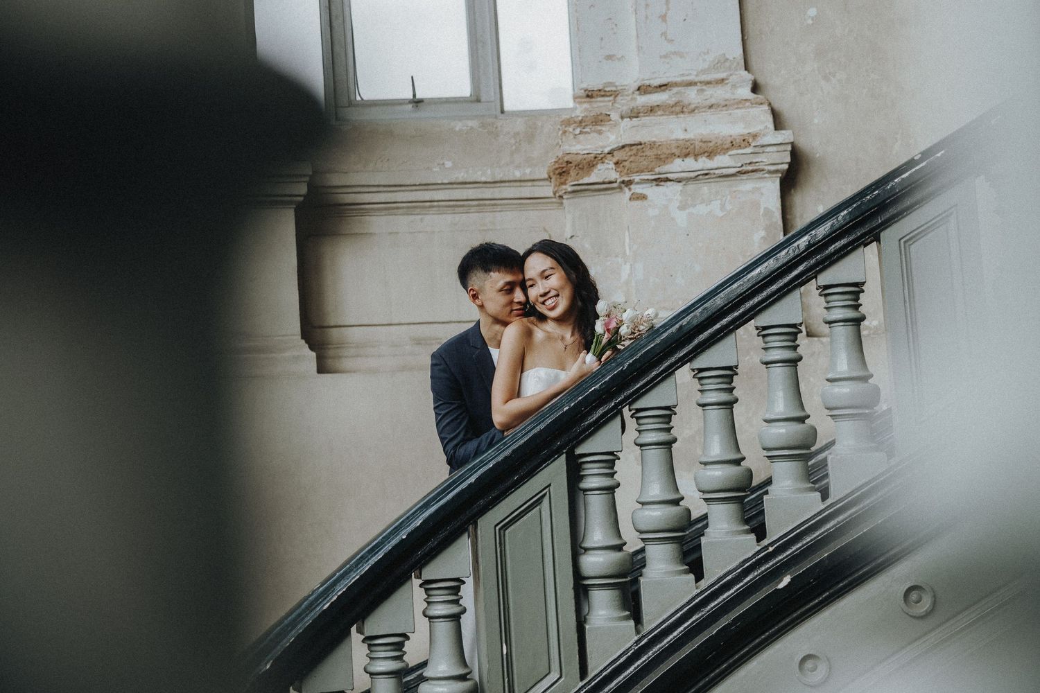 Couple shares romantic moment on elegant curved white staircase with vintage bannister.