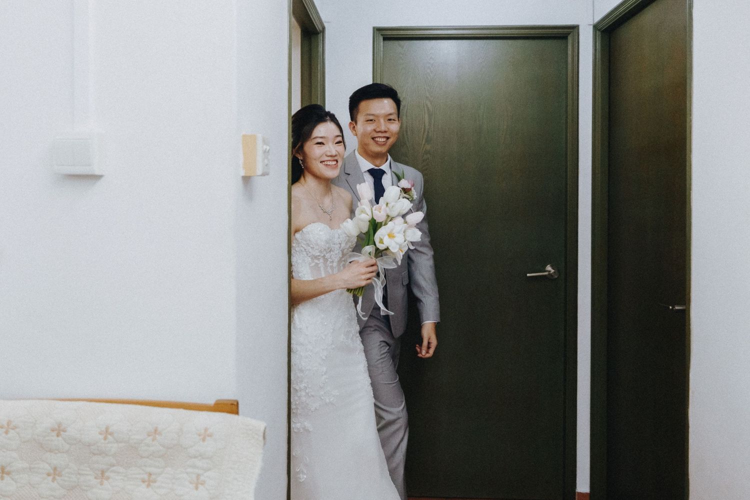 A couple in wedding attire stands together in a doorway holding a bouquet.