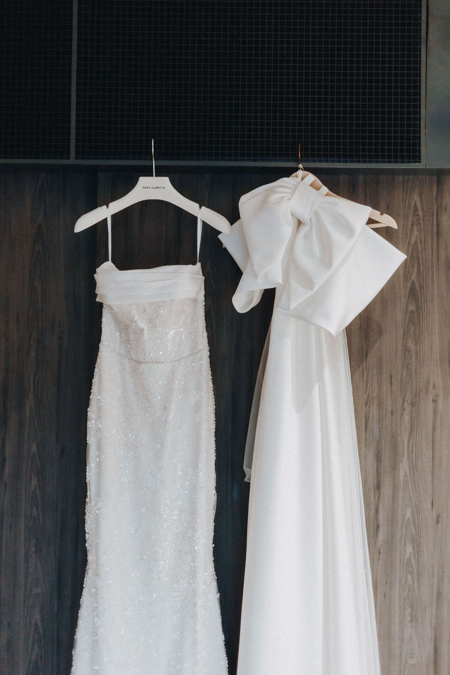 White wedding dresses hanging on display showcase delicate lace and elegant designs against a dark wood backdrop.