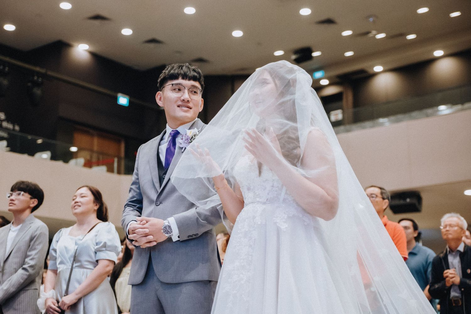 Wedding ceremony guests seated in rows watching celebration in modern indoor venue.