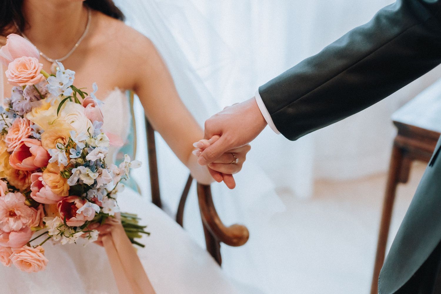 Bride and groom holding hands, with a colorful wedding bouquet of pink, peach, and blue flowers.
