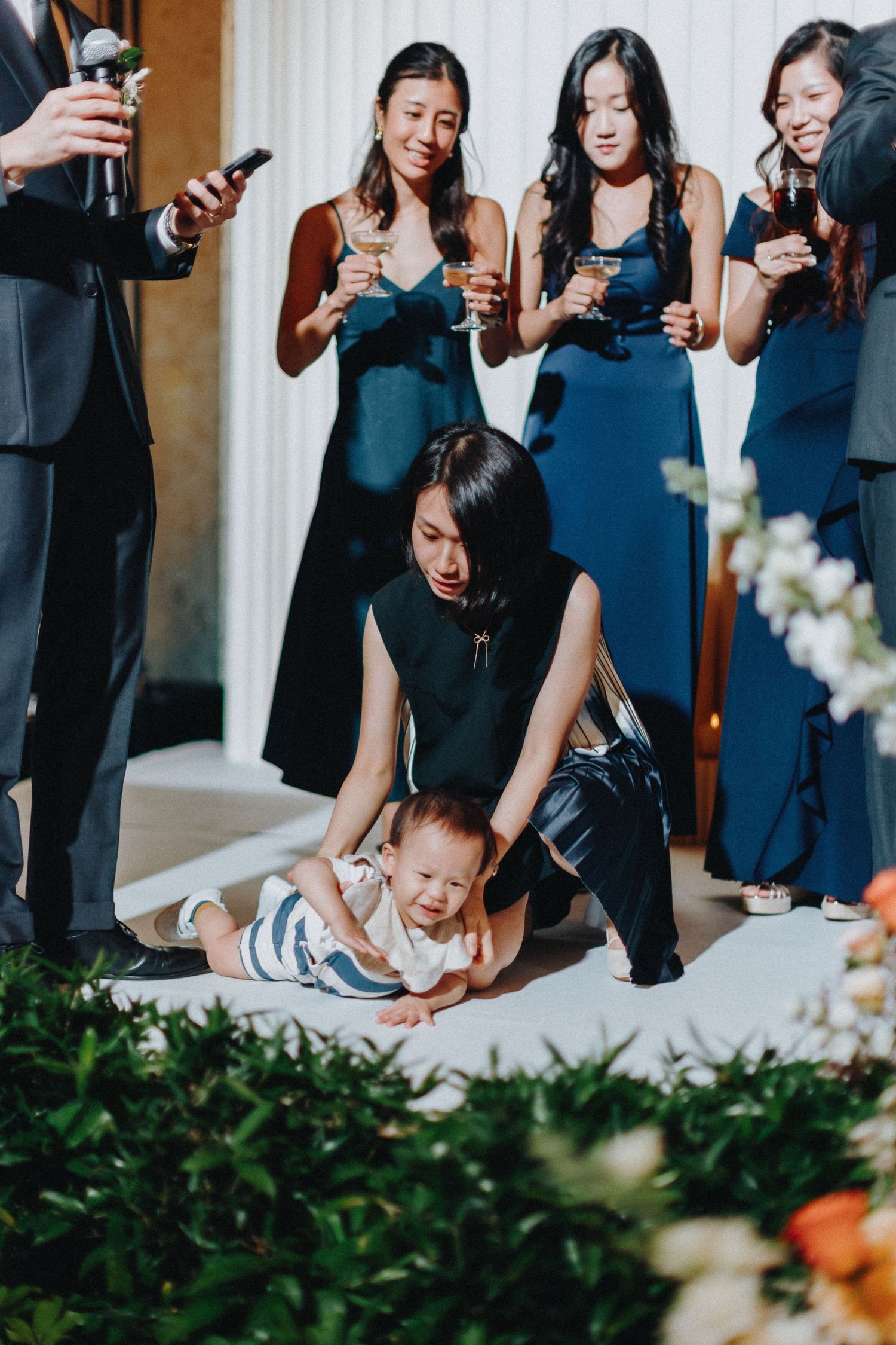 Wedding party in navy dresses gathered around a small child at reception.