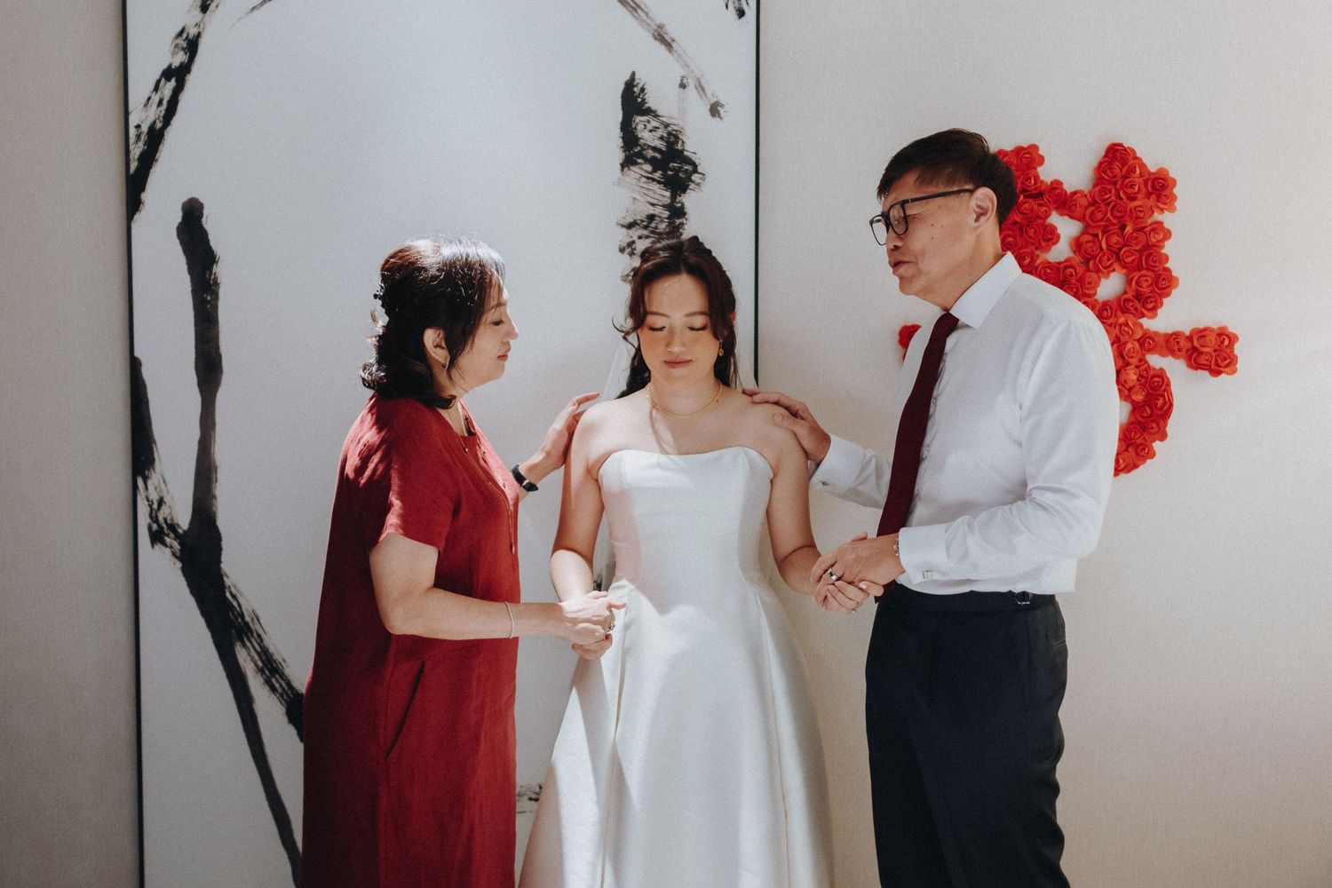 Candid moments between wedding party members against minimalist white wall with red flowers.