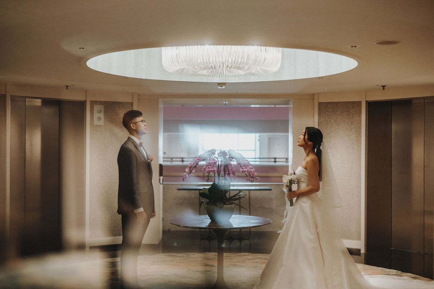An elegant hallway in a modern hotel features warm lighting and a large circular ceiling light fixture.