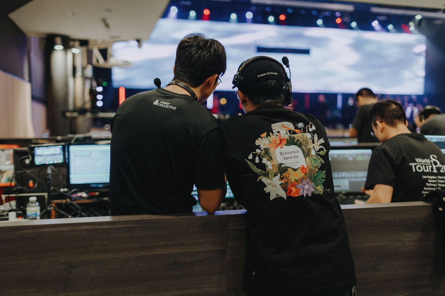Employees wearing black uniforms working at computer stations in a bar or restaurant with blue lighting.