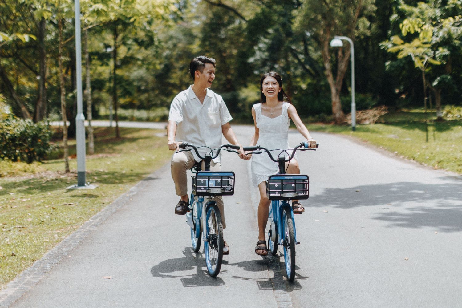 A cheerful couple riding blue rental bikes together on a sunny tree-lined path.
