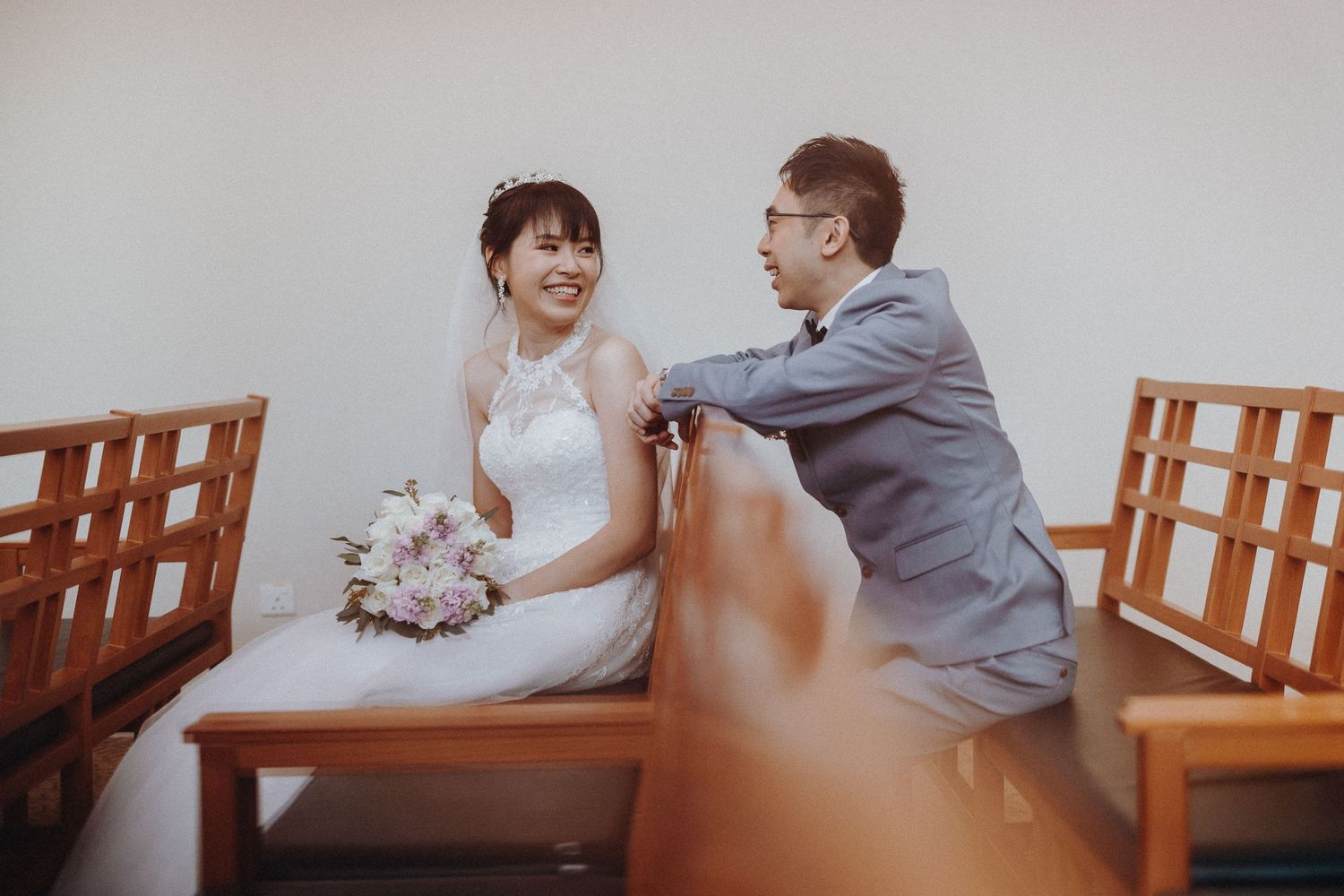 A couple seated on wooden pews sharing an intimate moment in a simple indoor setting.