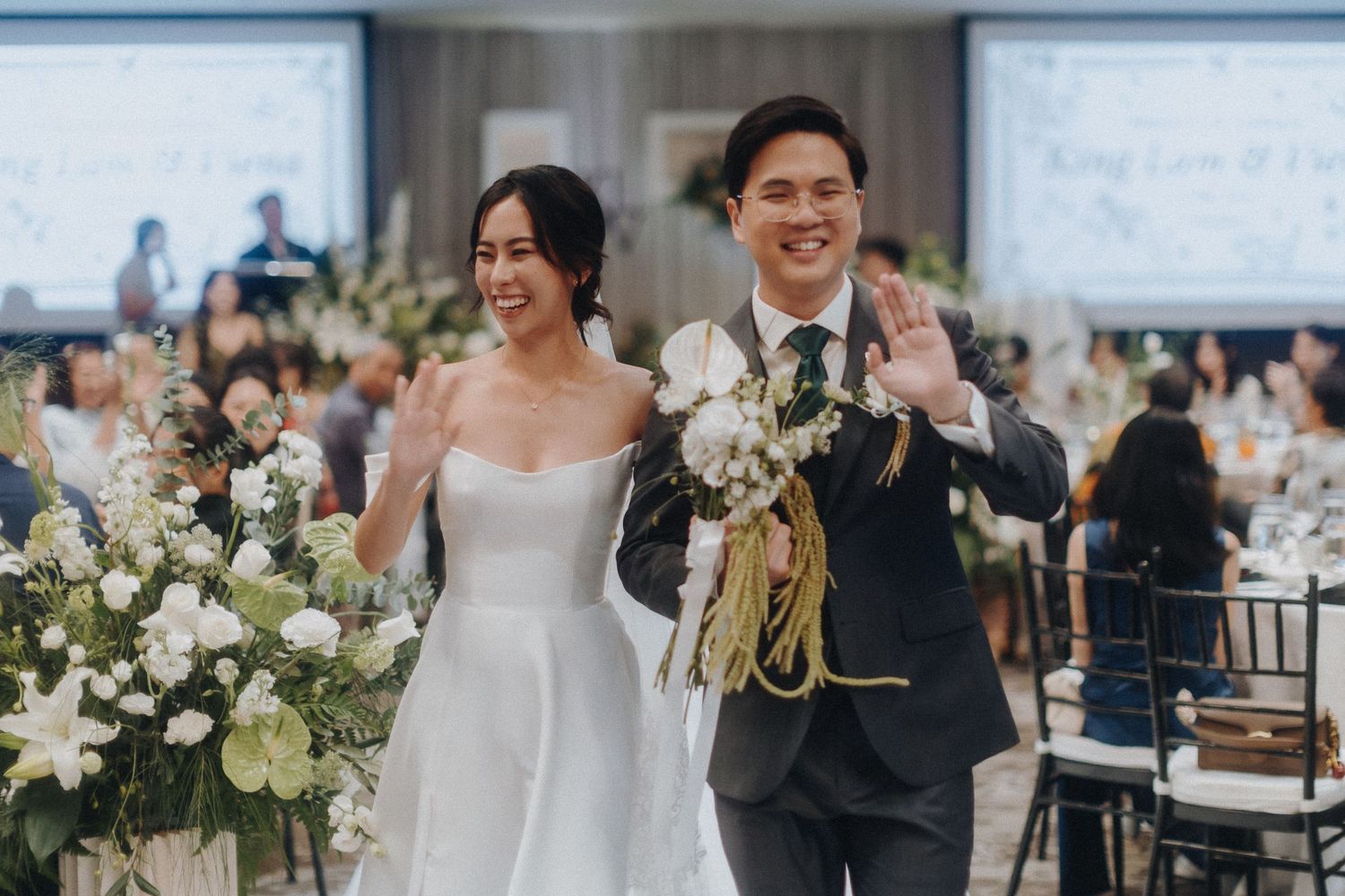 A newlywed couple celebrates during their wedding reception surrounded by white floral decorations.