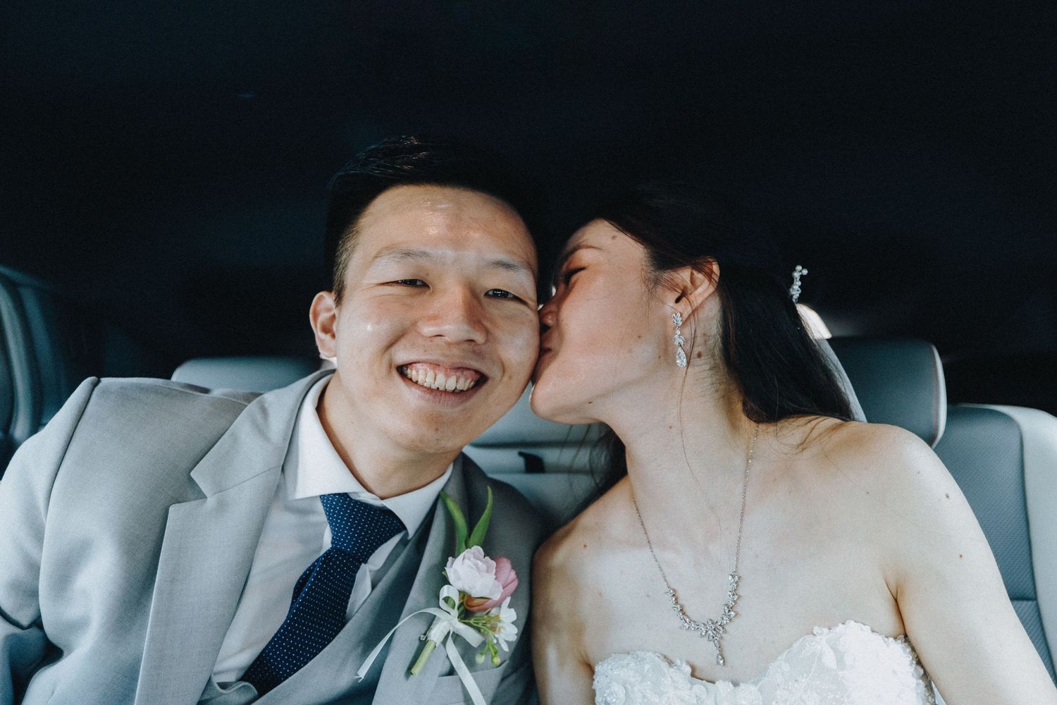 Newlyweds share an intimate moment in the back seat of a car with natural lighting.