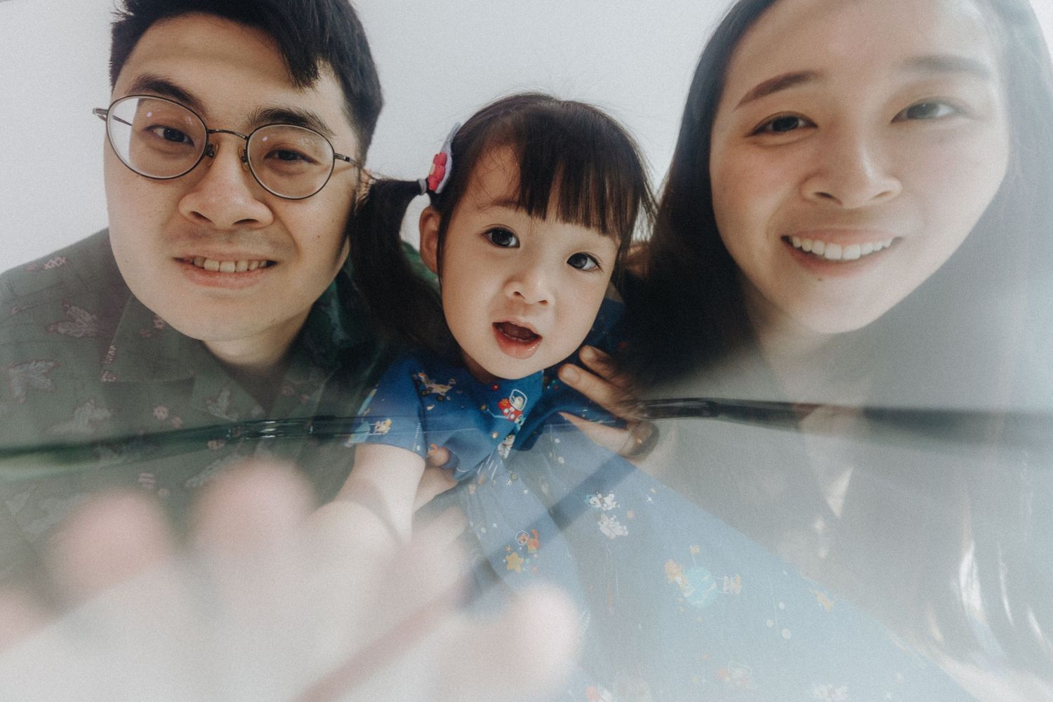 Close-up selfie style family portrait with child in denim dress.