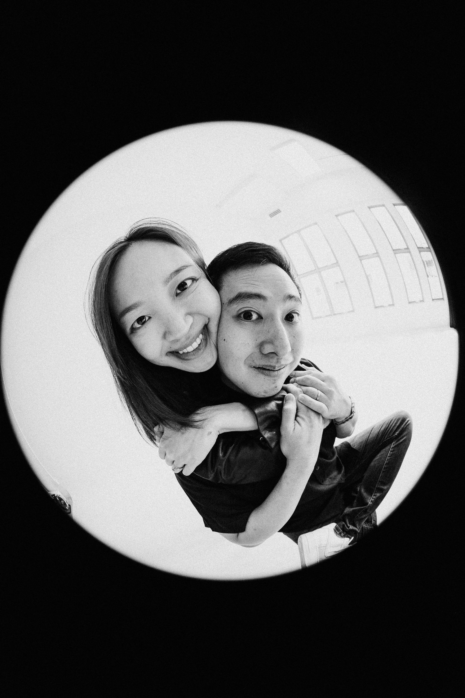 A circular fisheye portrait captures a couple sharing a close embrace in black and white.