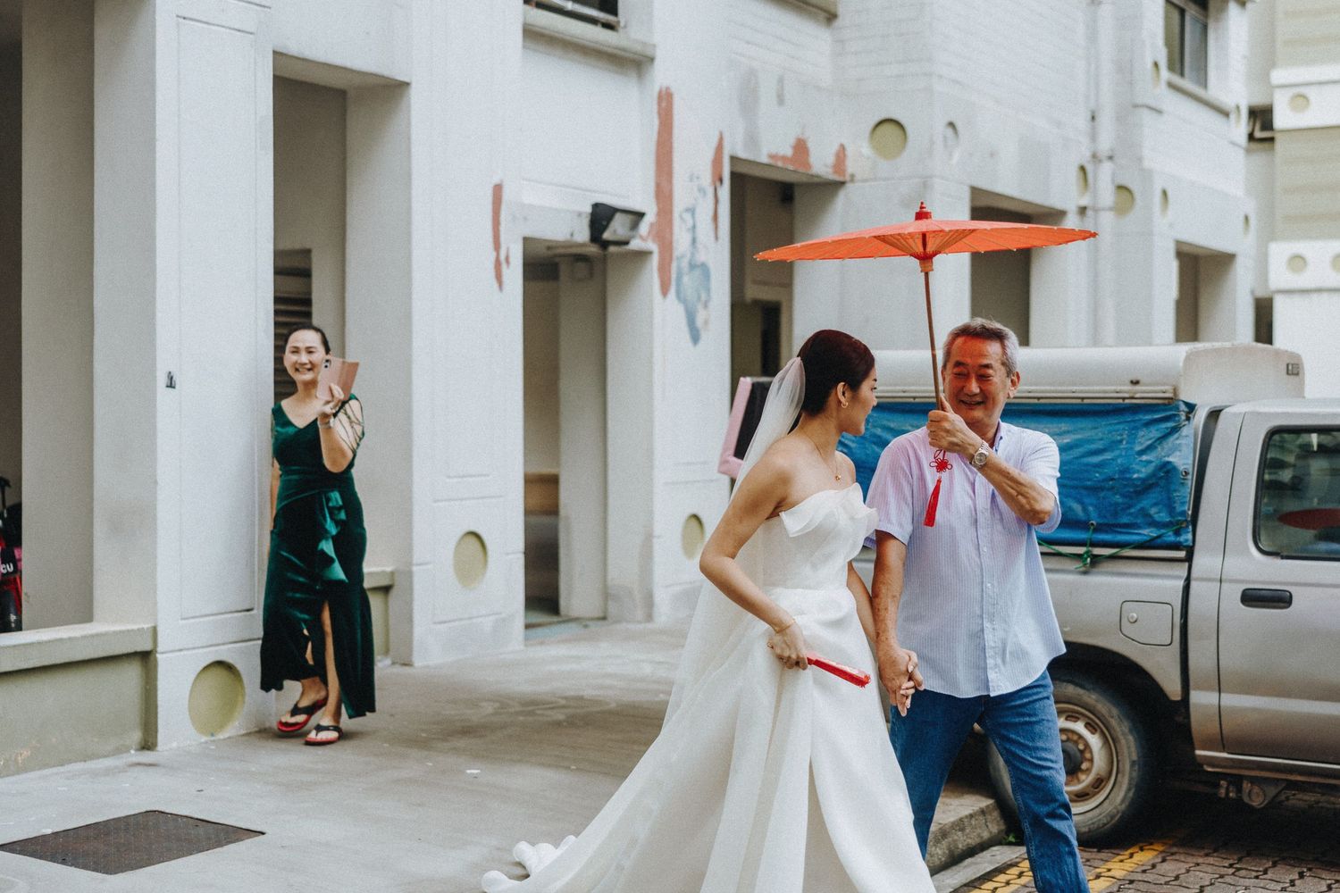 A bride in a white wedding dress walks down a street while others watch from nearby.
