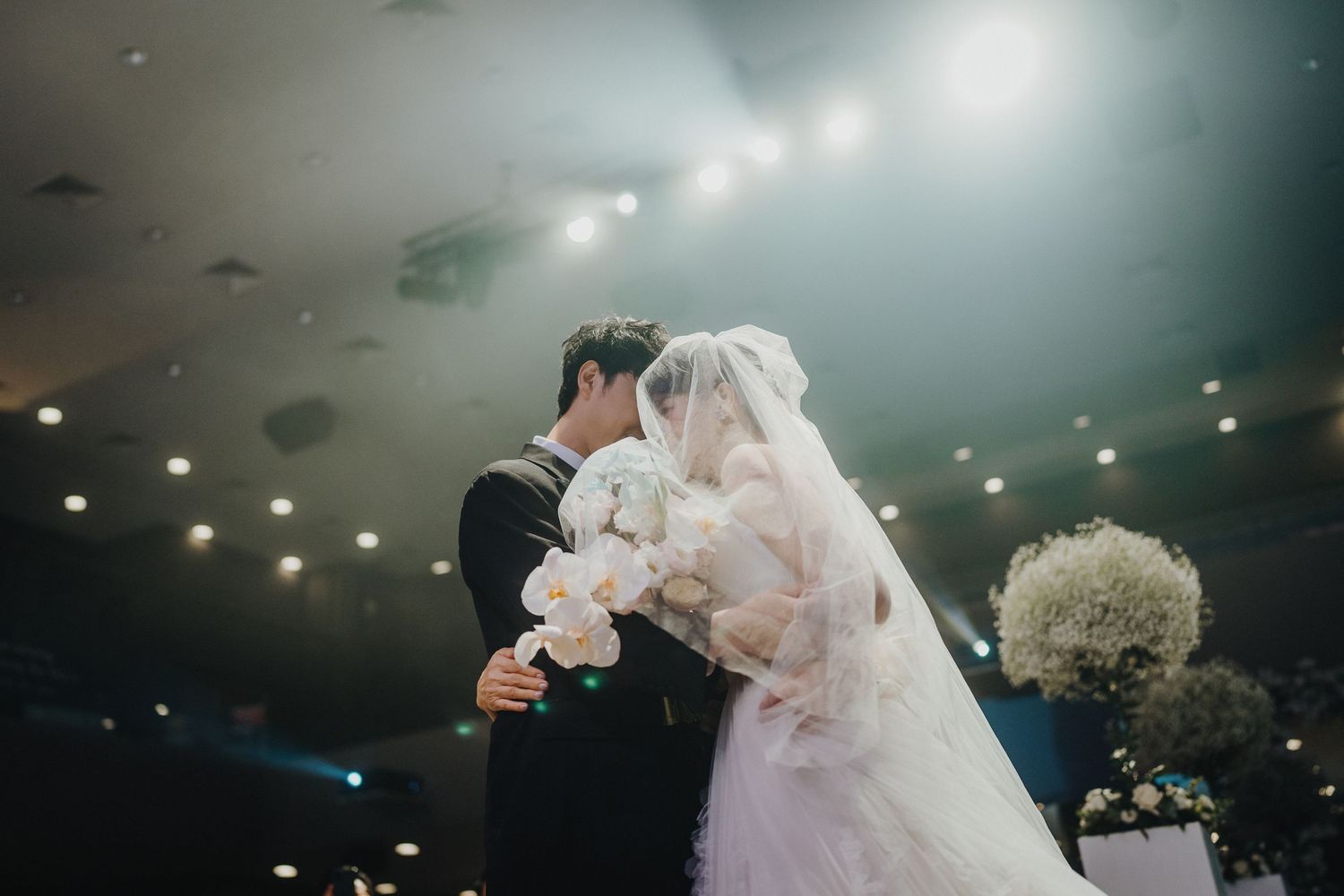 Wedding ceremony moment with white bouquet and veil under dramatic lighting.