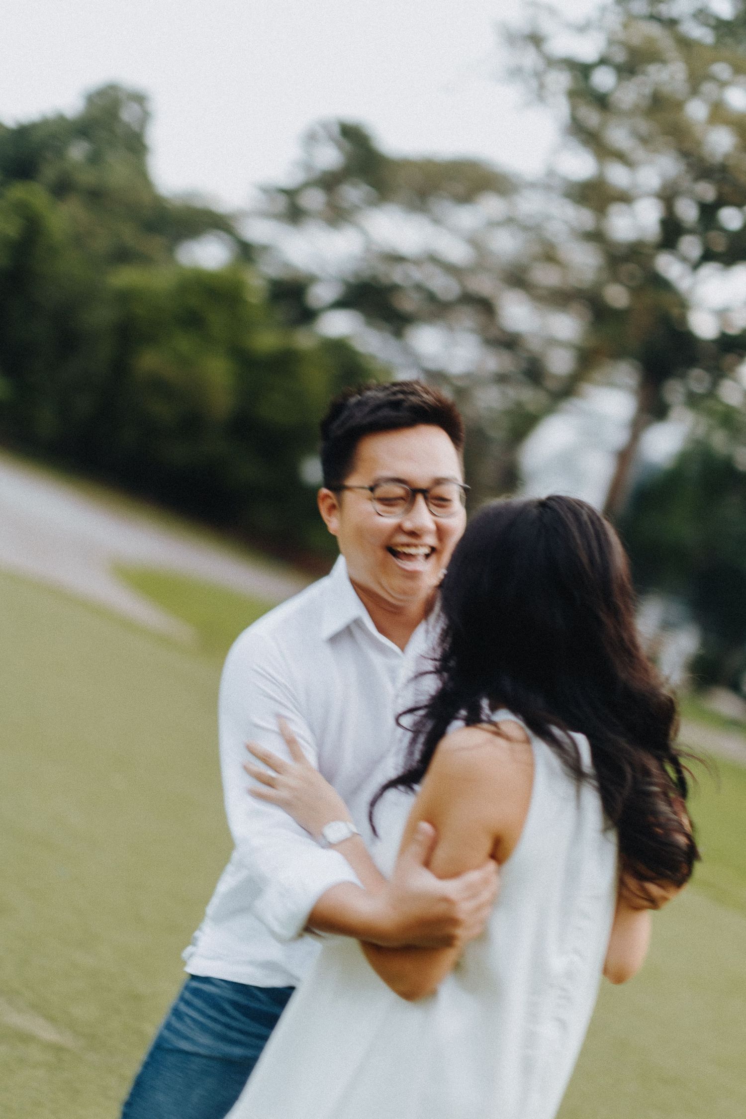 A couple shares a joyful moment laughing together outdoors on a grassy field.