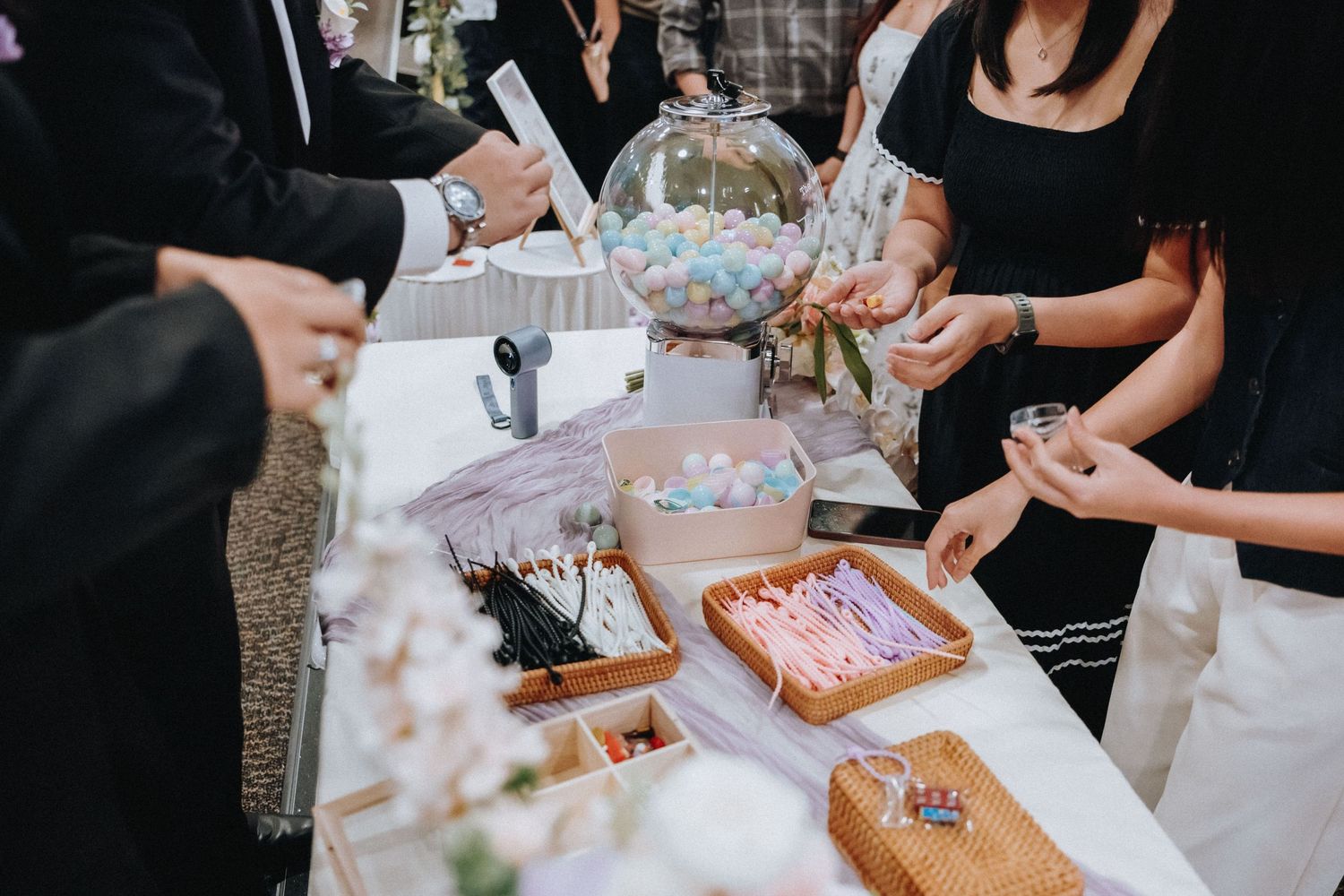 Guests reaching for party favors and gifts displayed on a white-clothed table at a wedding reception.