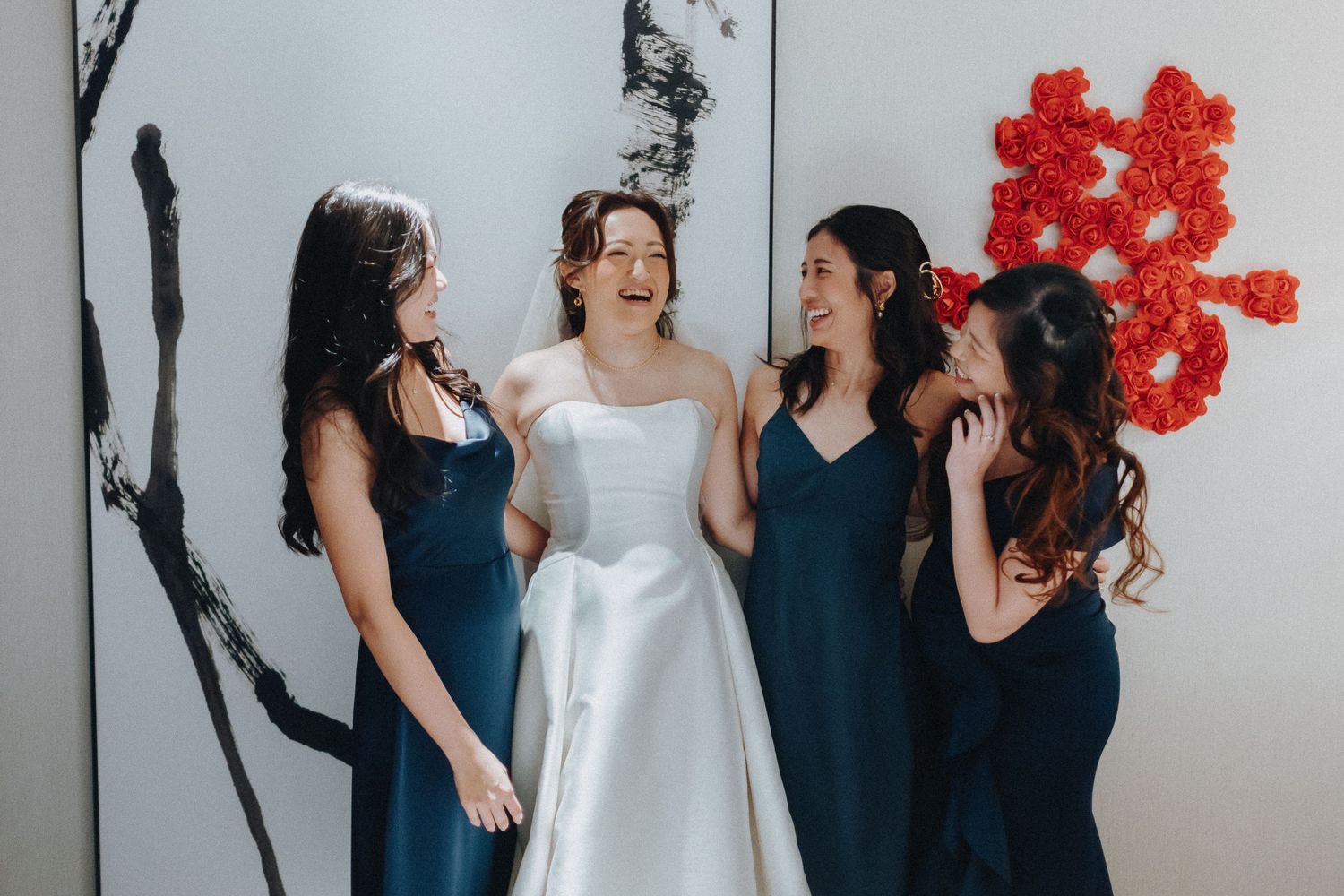 Elegant wedding party gathering in navy and white attire against minimalist backdrop with red flowers.
