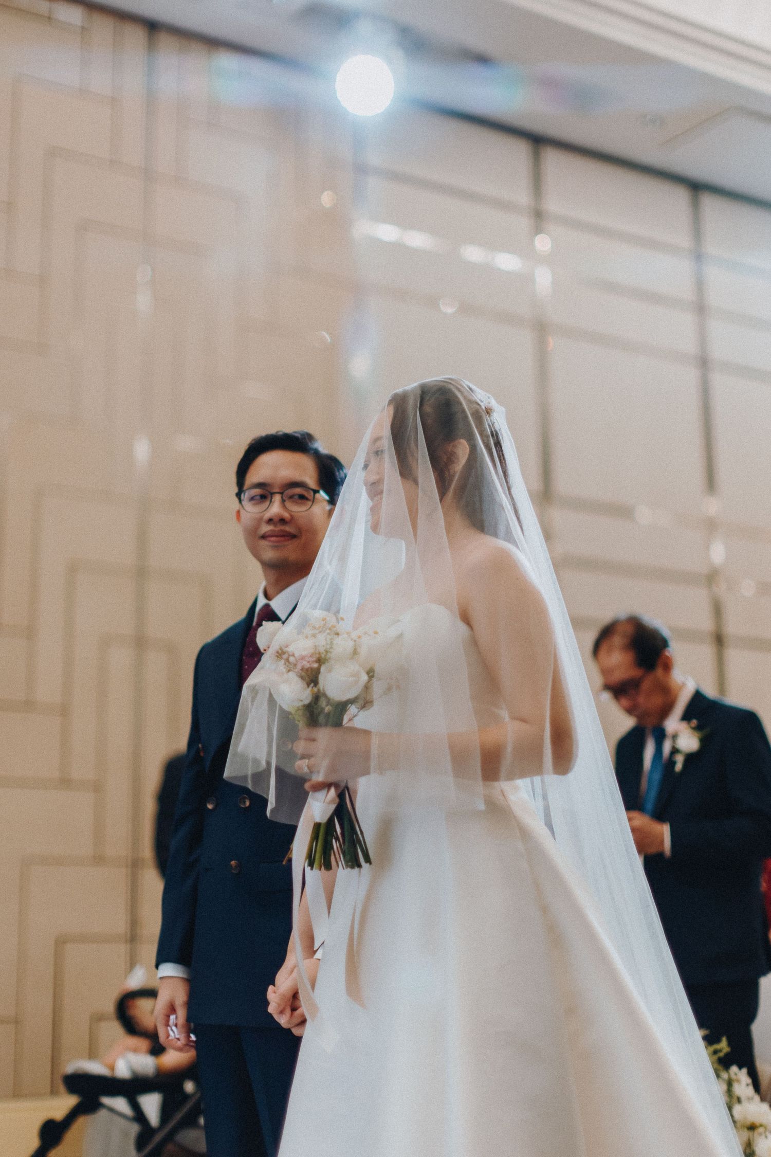 Bride in white gown and veil walks down the aisle at an elegant venue.