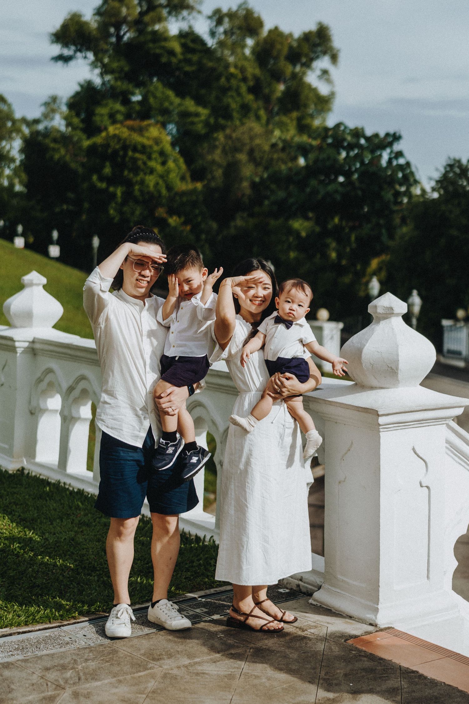 Three friends enjoying a playful moment peeking through white pillars at a scenic outdoor location in matching casual outfits.
