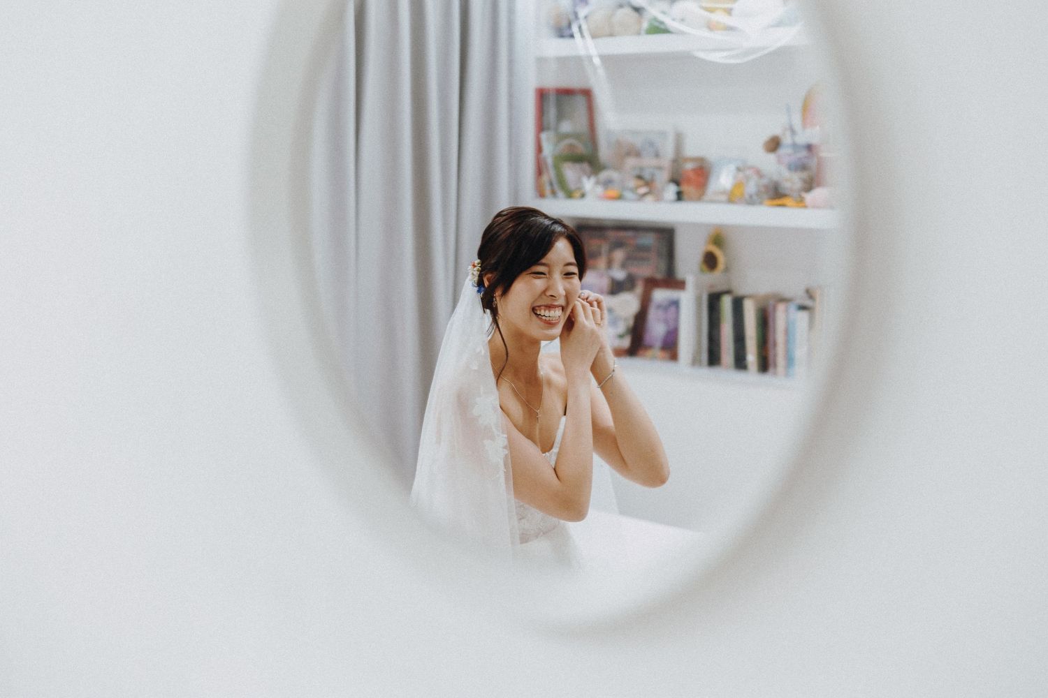 A person in white wears jewelry while doing a beauty routine in front of a bathroom mirror.