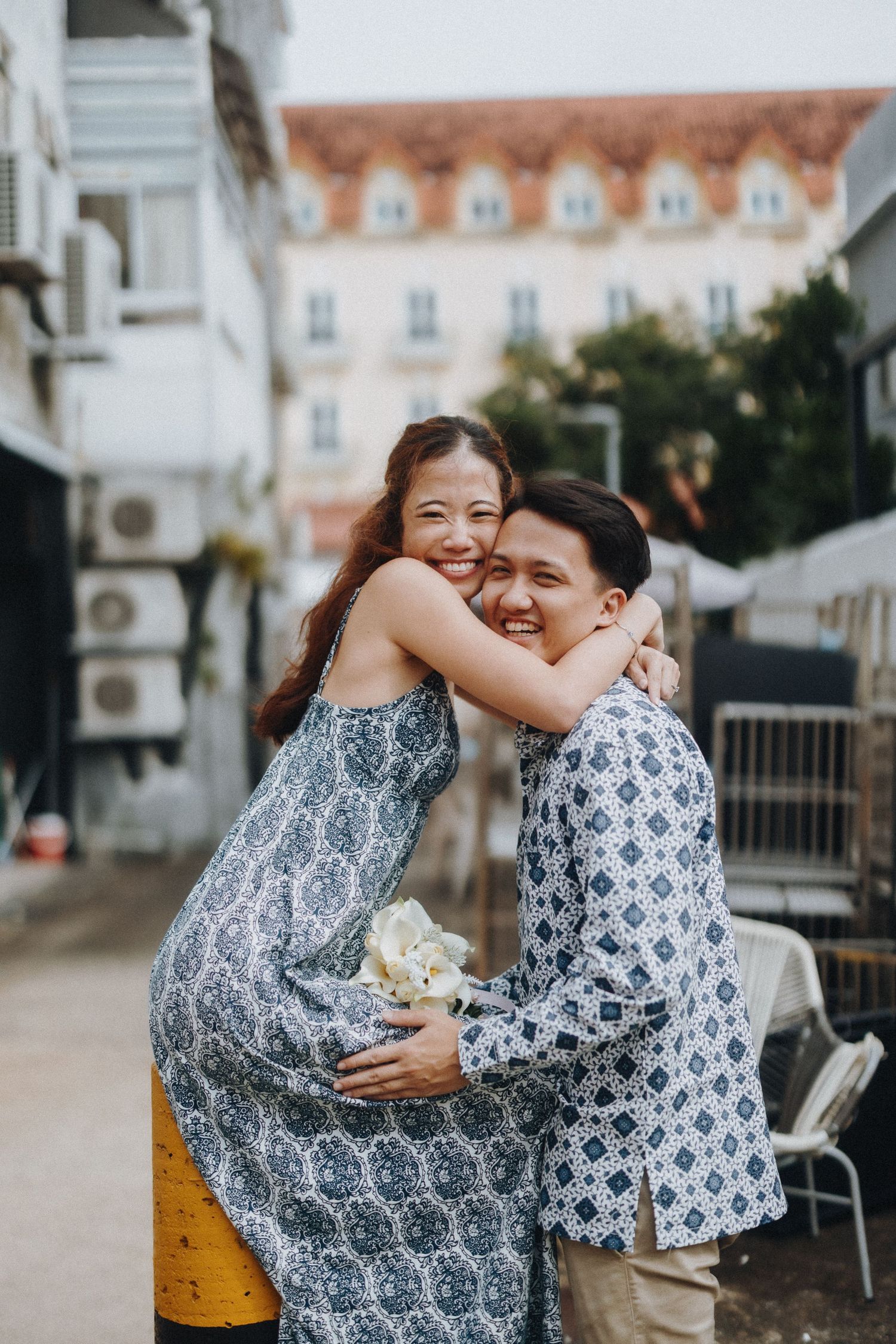 A joyful couple in matching blue and white patterned outfits embrace and laugh together outdoors.
