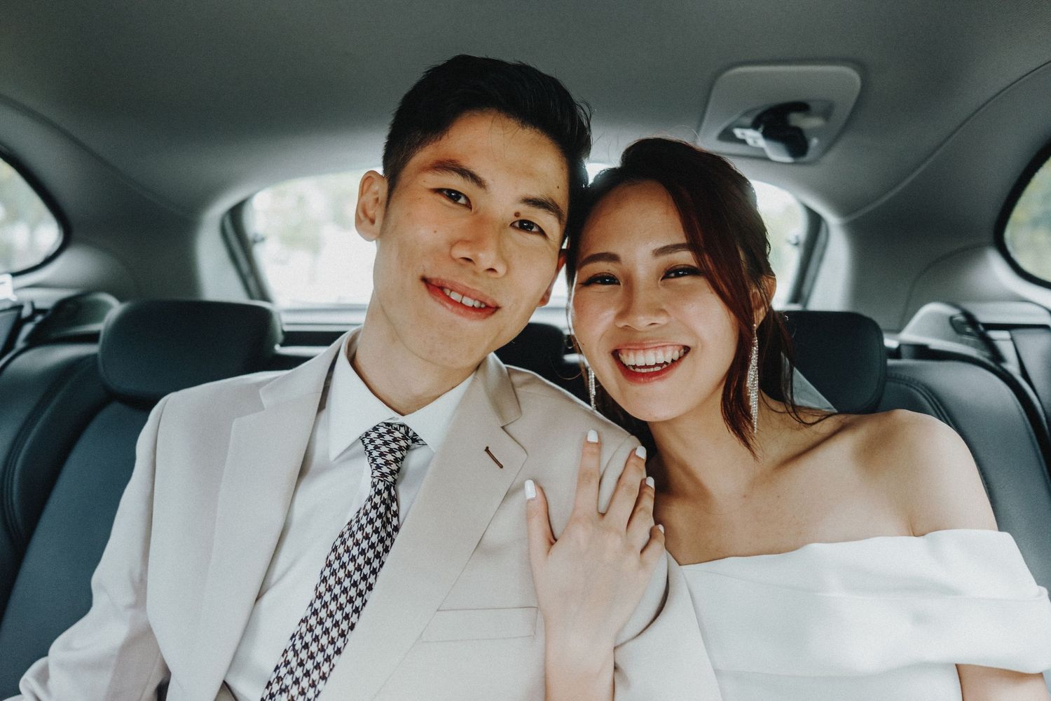A happy couple smiles and shares tender moments together in a wedding car wearing white formal attire.