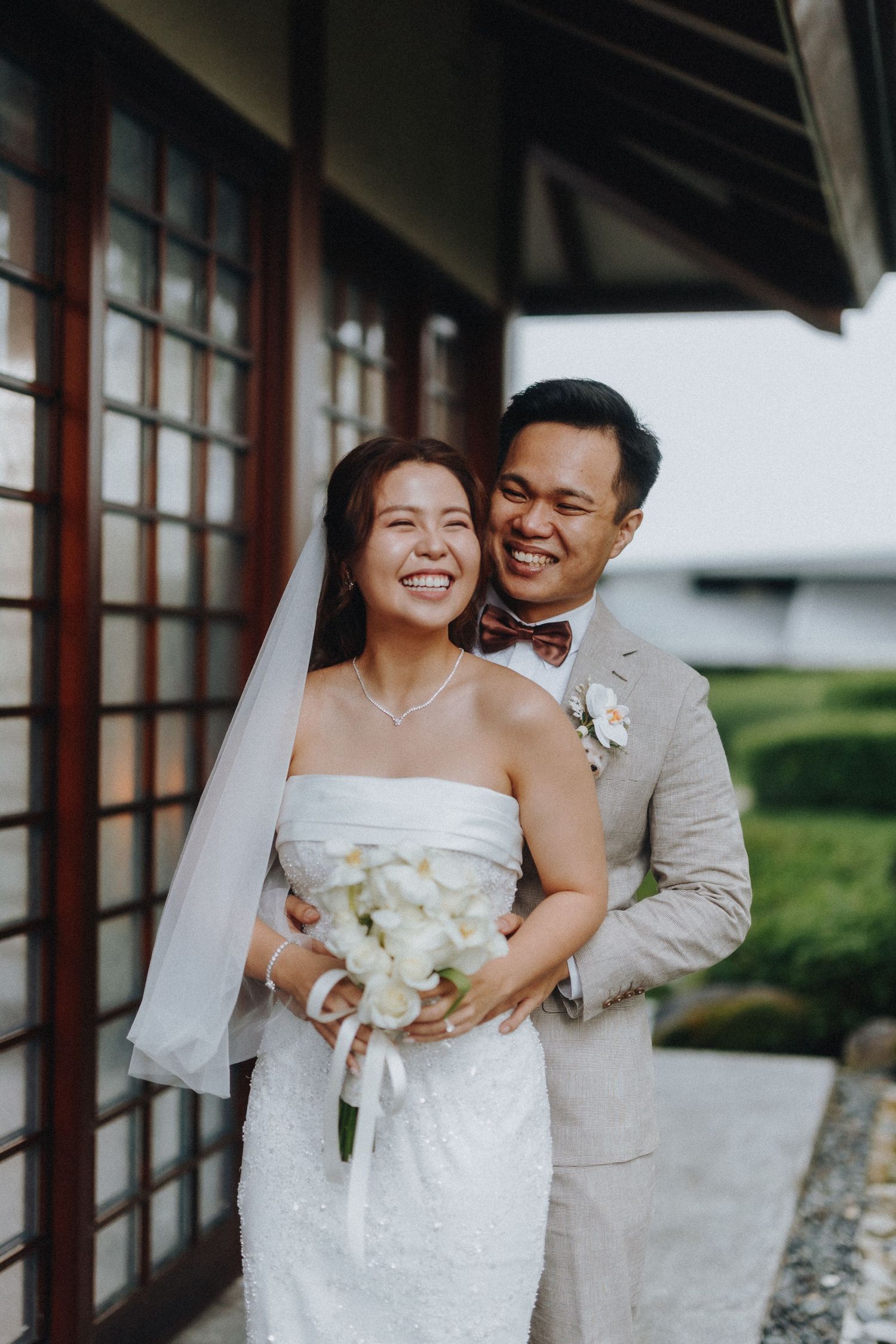 Joyful wedding couple sharing an intimate moment beside traditional Japanese screens and windows.