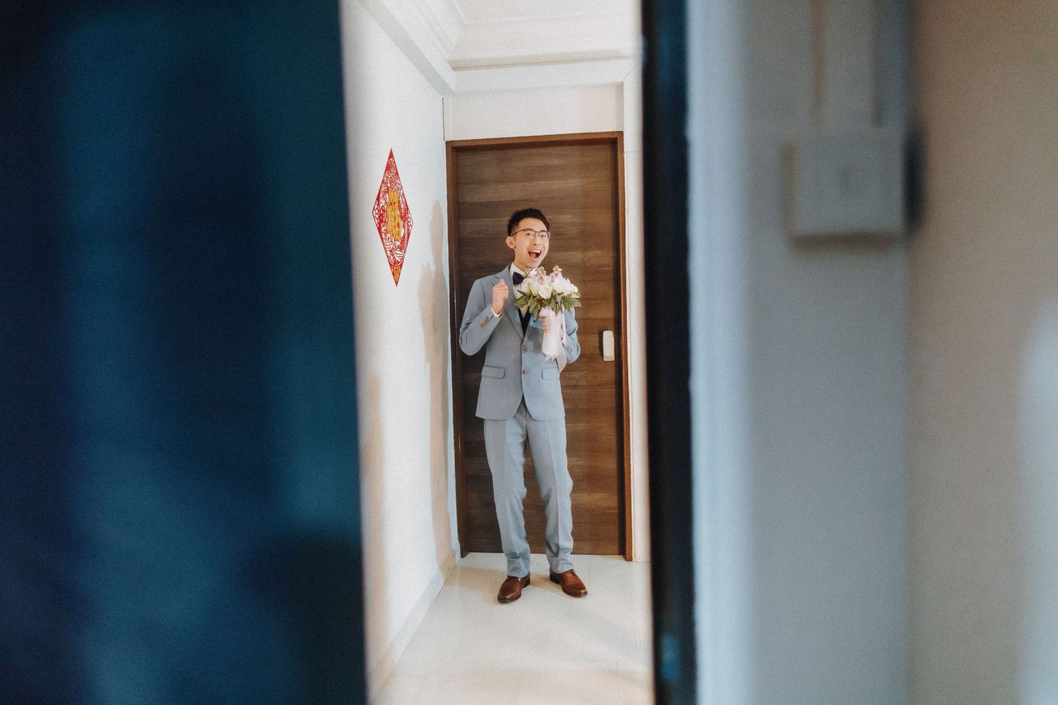 A glimpse through a doorway of someone in a light gray suit adjusting their tie.