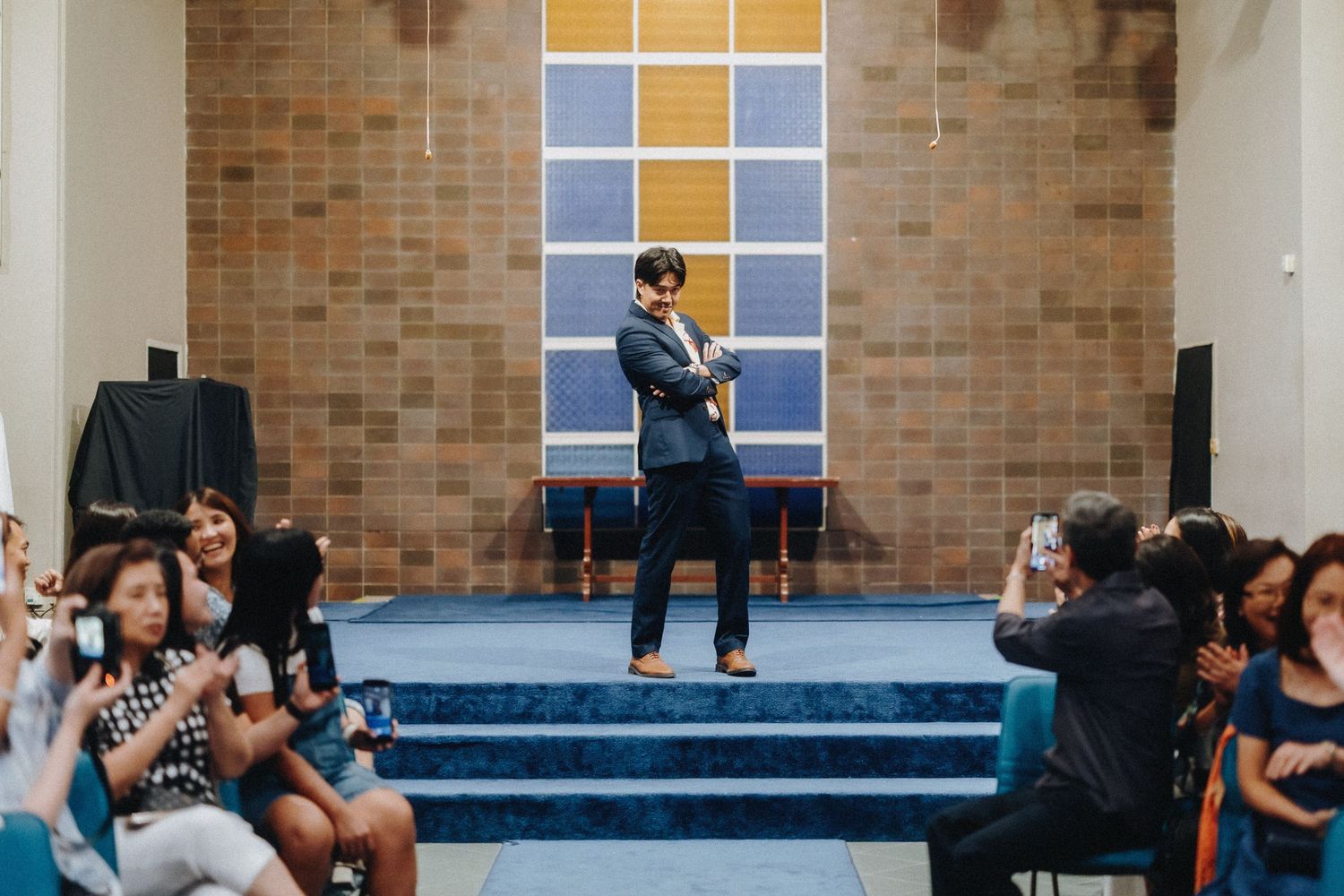 Group gathering in a brick-walled room with blue stage and window panels.