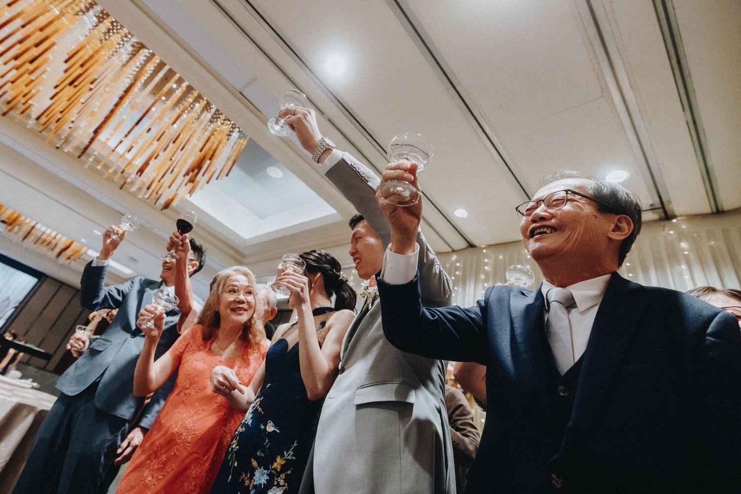 People in formal attire gathered in a room with warm lighting and decorative ceiling details.