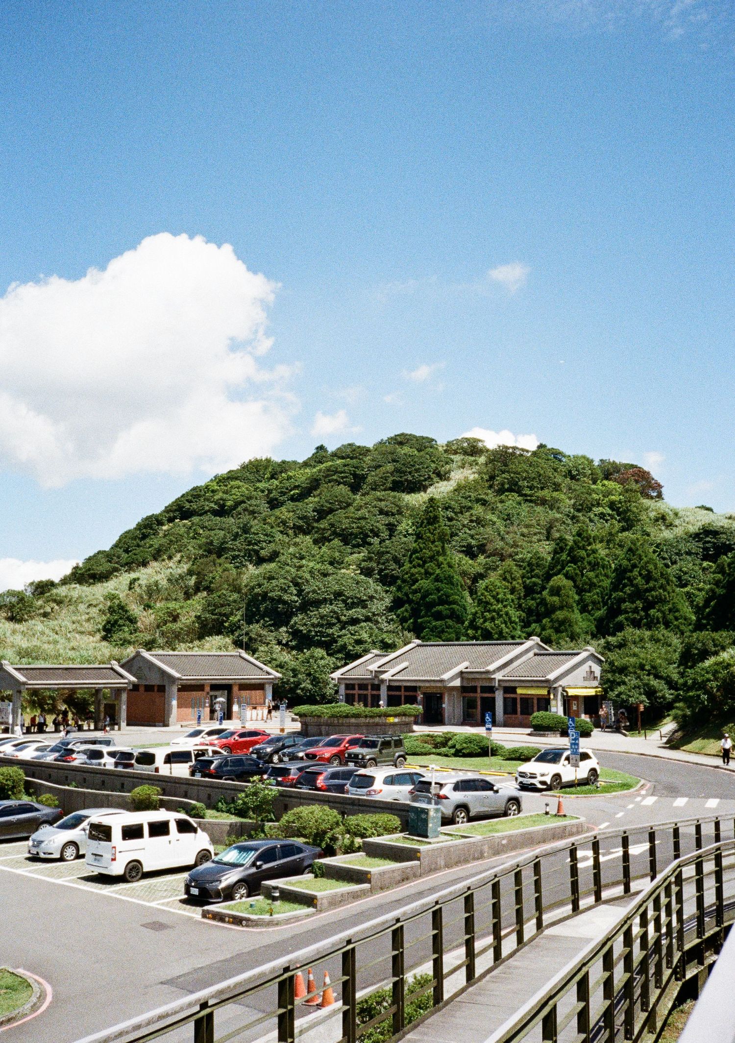 Modern seaside parking lot with wooden railing overlooking green hills and visitor facilities.