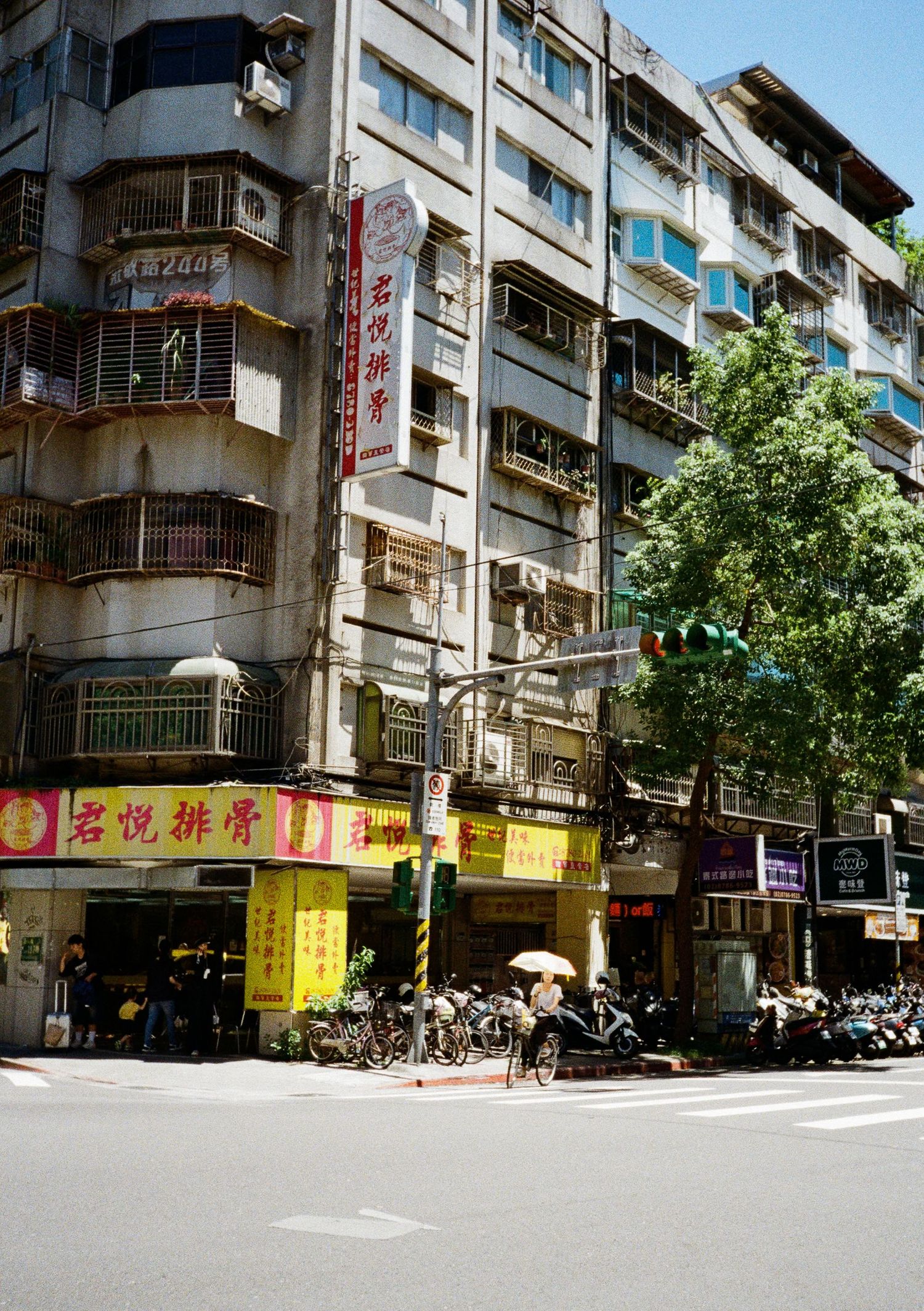 Urban street scene in Taiwan with yellow storefront signs and apartment buildings on a sunny day.