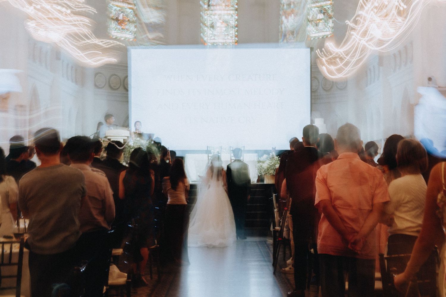 Guests stand in church pews as a bride walks down the aisle toward a glowing altar during a wedding ceremony.