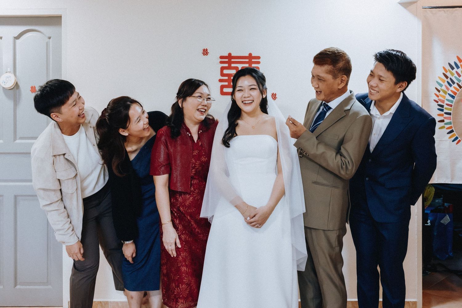 Joyful bride in white dress celebrates with smiling family members in front of Chinese wedding decor.