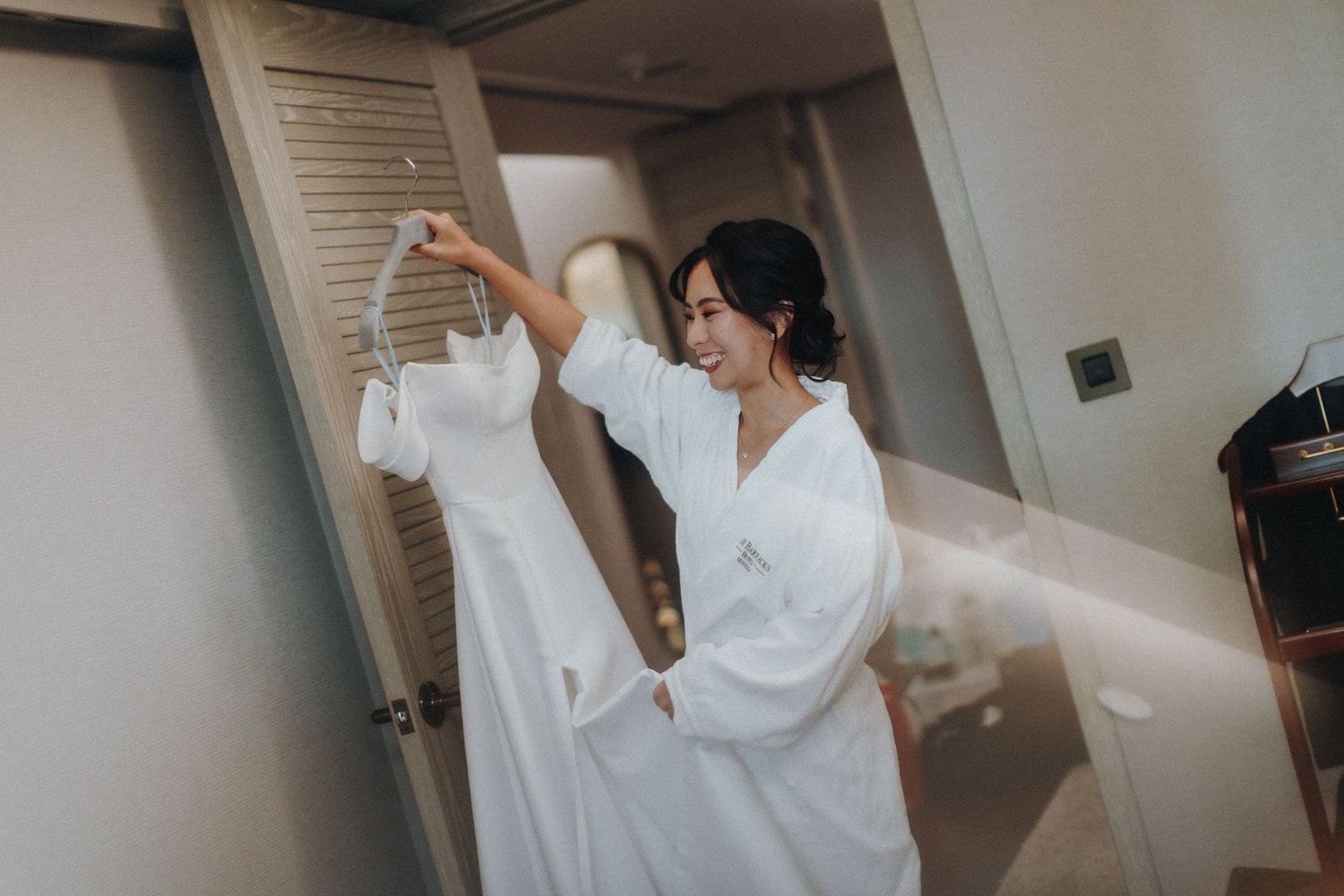 A person in a white robe hangs up a white wedding dress in a hotel room during preparations.