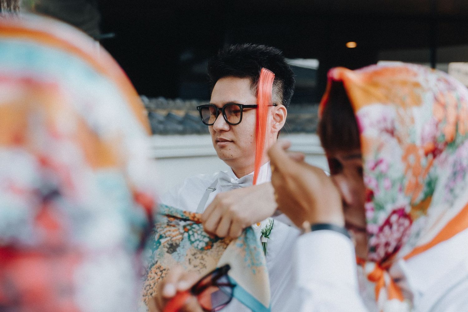 A group of people participate in a colorful cultural celebration wearing traditional Asian garments and accessories.