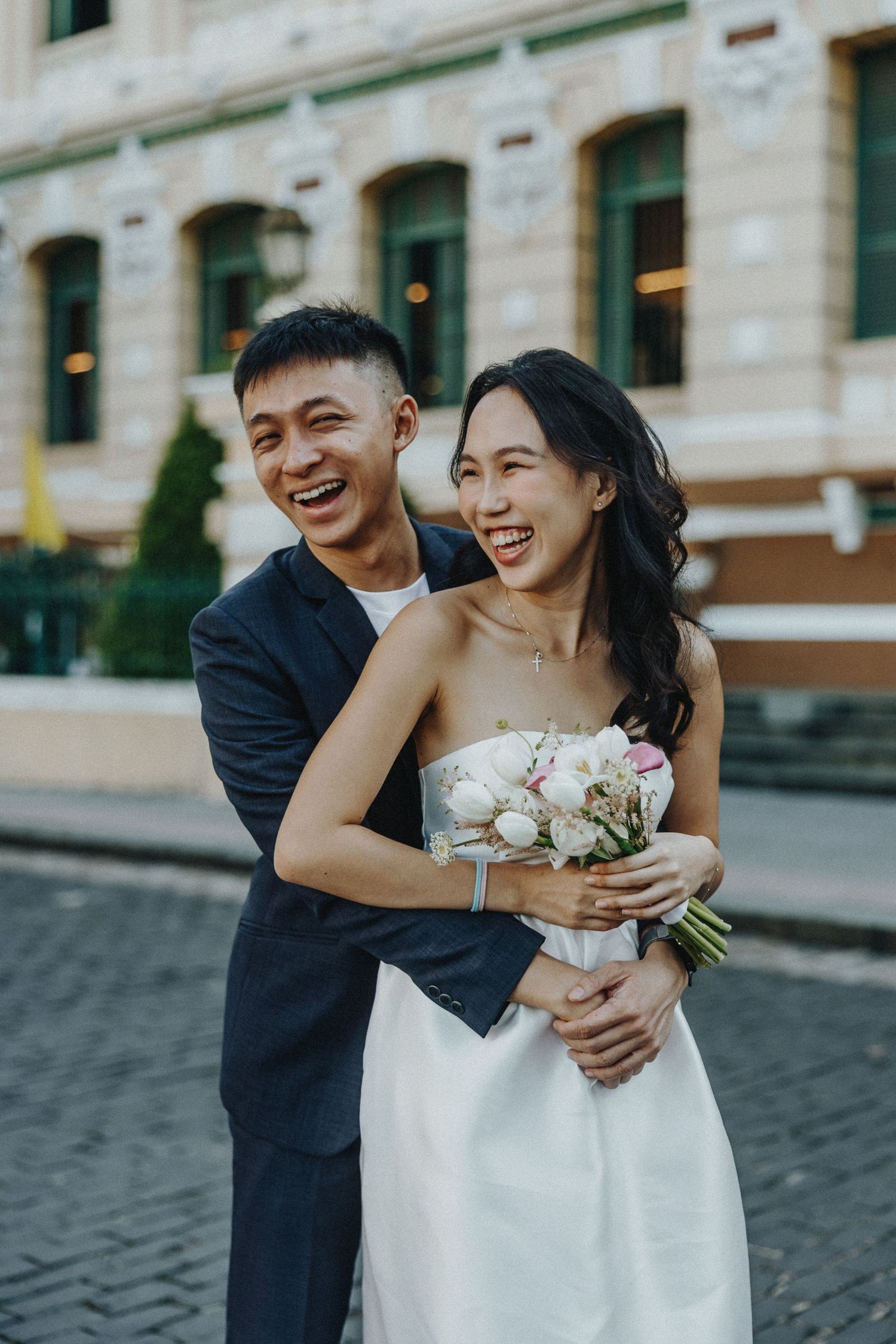 Romantic wedding couple shares intimate laughs and embraces while posing for photos on cobblestone street.